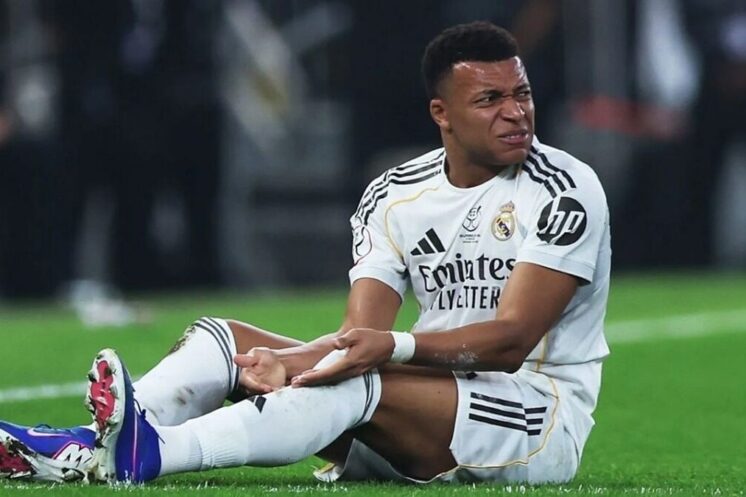 Kylian Mbappé assis sur la pelouse après une douleur au genou.